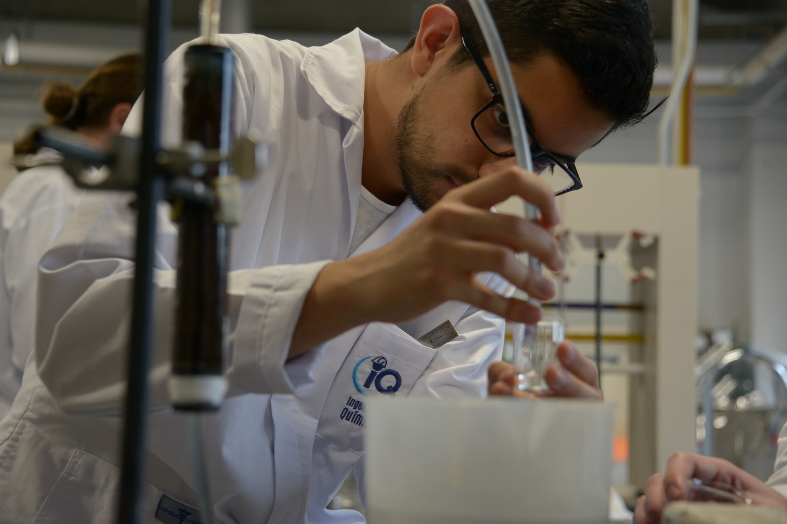 Se muestra un estudiante en desarrollando un proyecto en un laboratorio químico usando tubos y envases de vidrio
